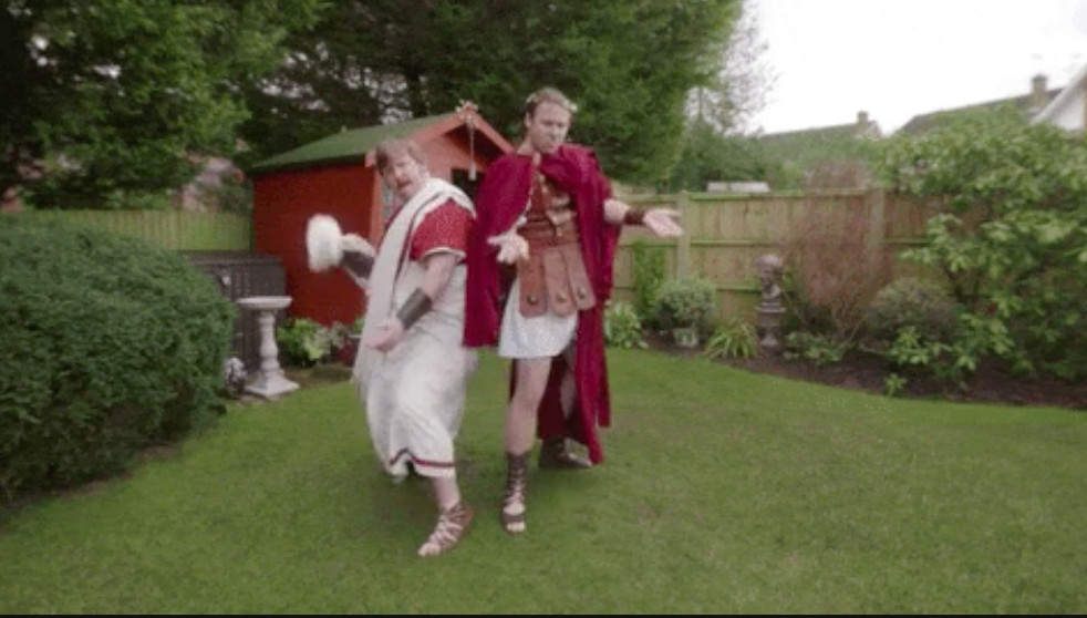 Photograph depicting two grown men posing in Roman period costumes in a backyard